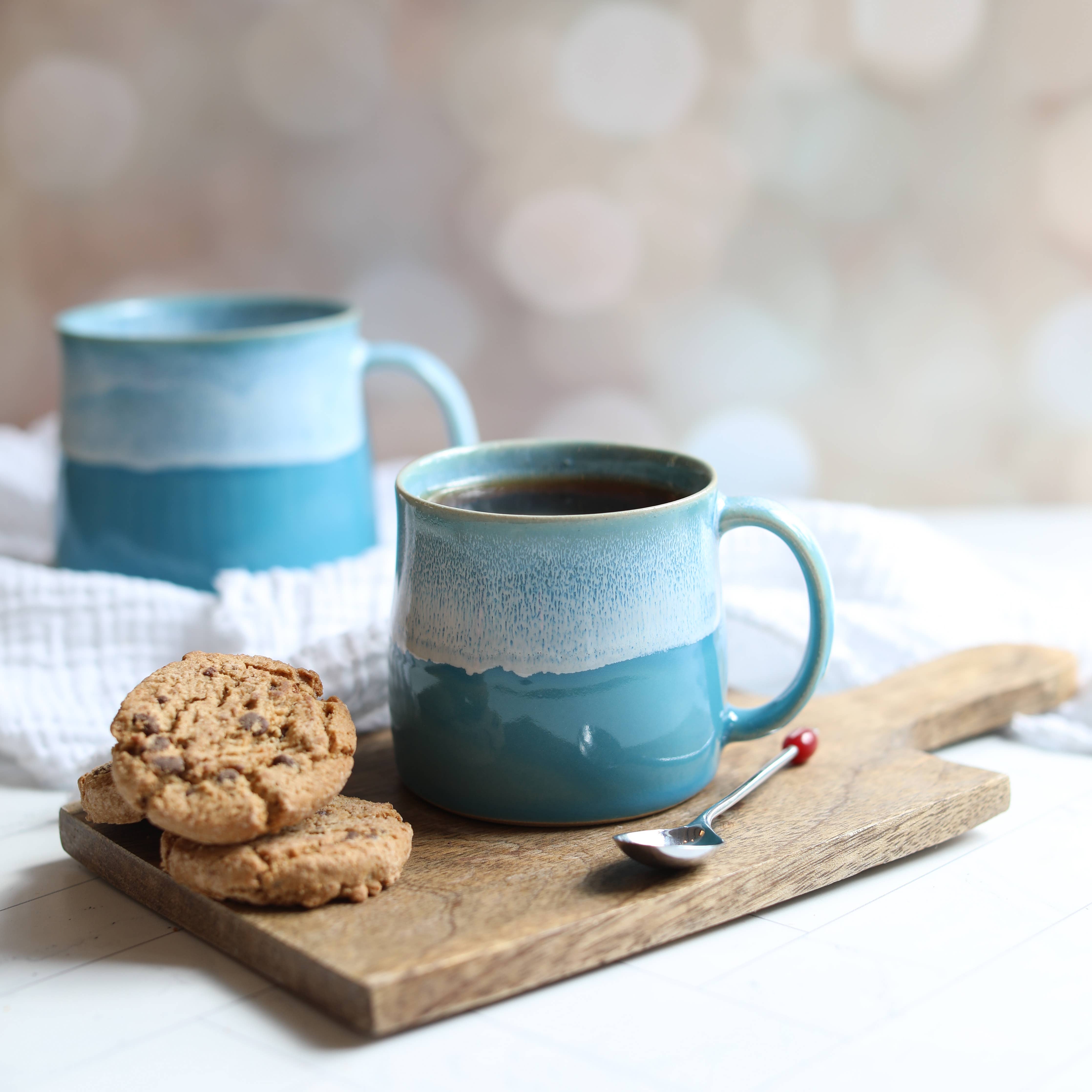 Two blue ceramic mugs with white accents on a wooden tray with cookies and a spoon.