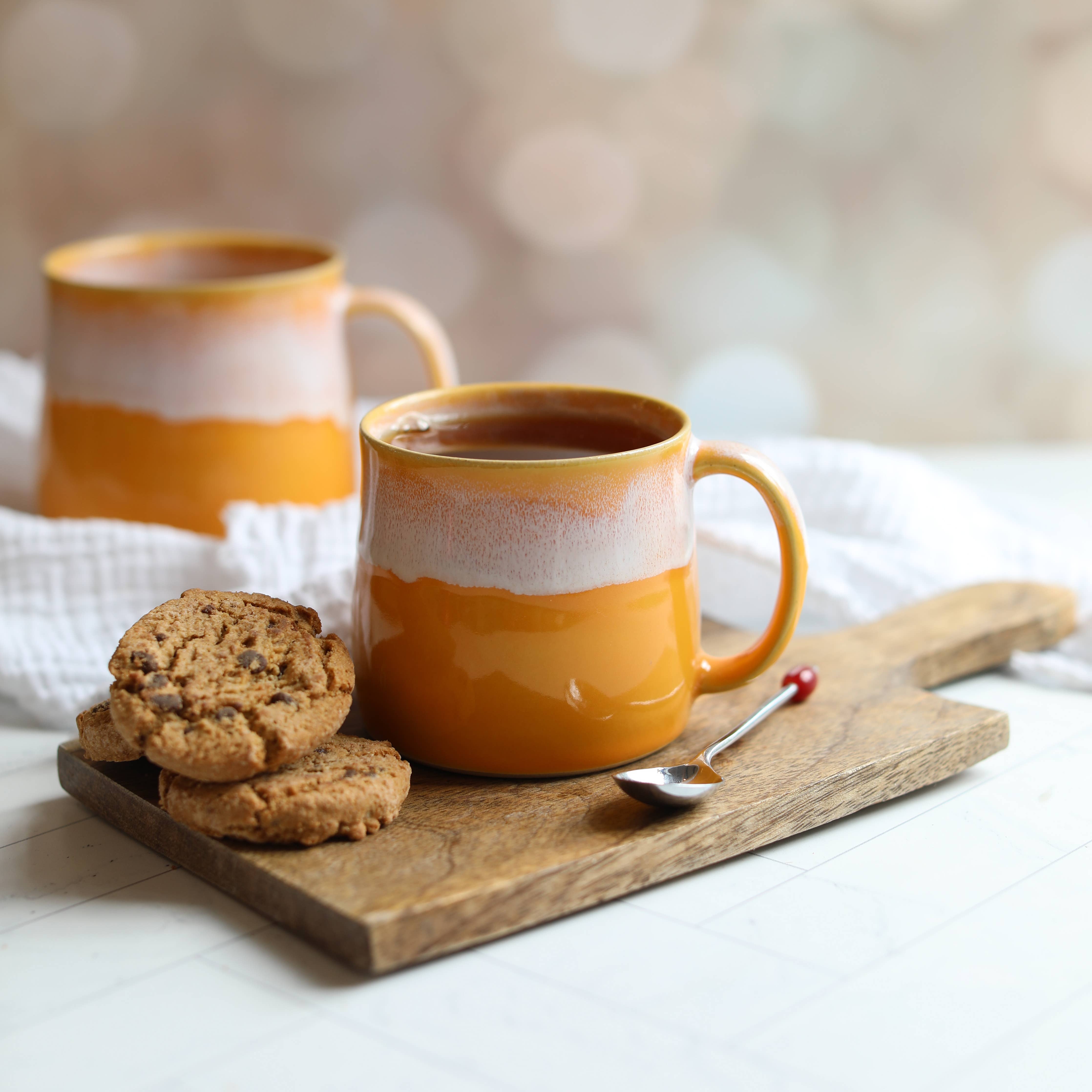 Two orange mugs with white accents on a wooden tray with cookies and a spoon.