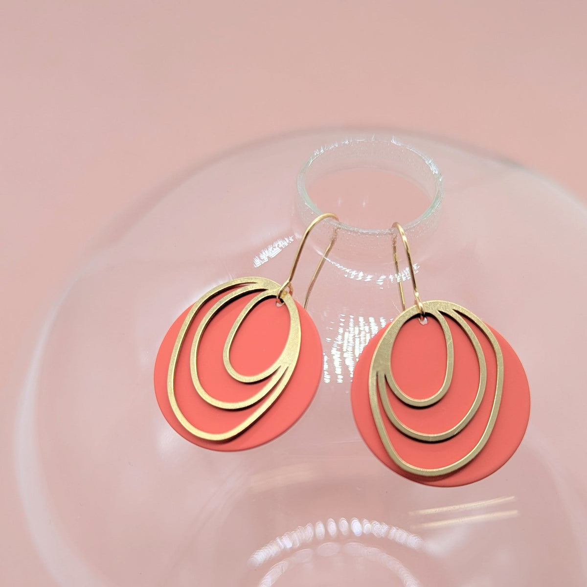 Coral earrings with gold circular designs on a pink background