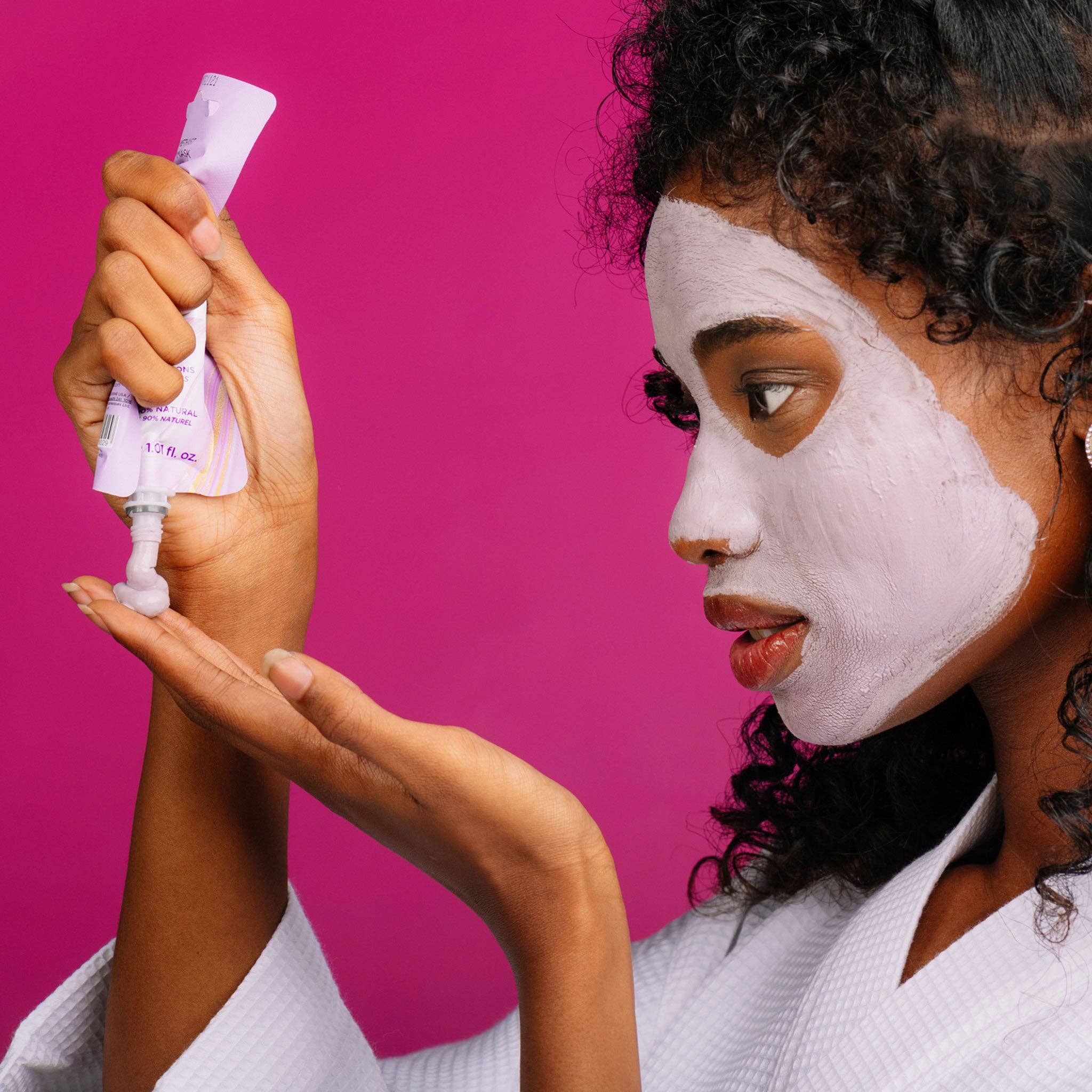Woman applying a facial mask with a pink background