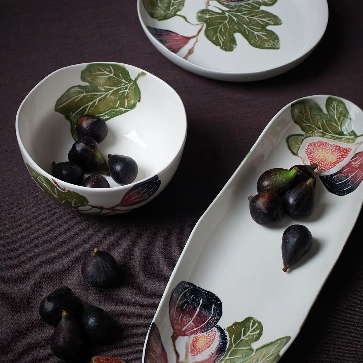 Decorative ceramic bowls and platter with fig illustrations on a dark surface